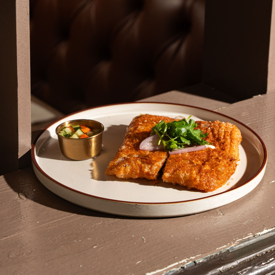 Crispy golden fried fillets garnished with cilantro and red onion, served with a cup of pickled vegetables on a plate.