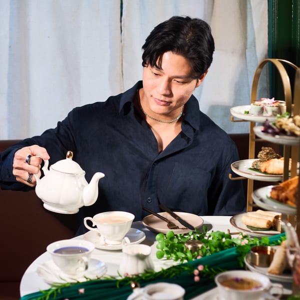 A man pours tea from a white teapot into a cup at a table with Thai appetizers.