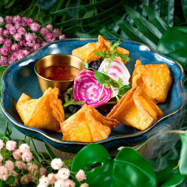 Golden fried Thai wontons with dipping sauce, garnished with colorful radishes and greens on a blue plate.