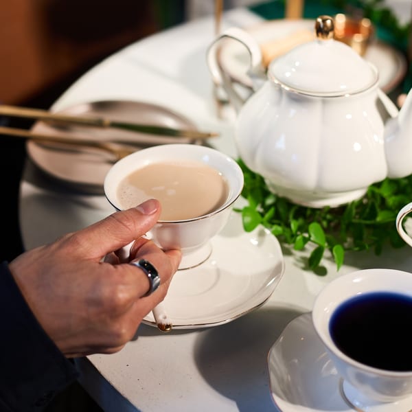 A hand holding a cup of Thai iced tea next to a teapot and another blue drink.