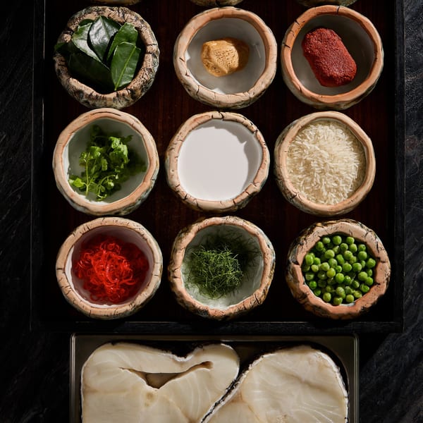 Overhead view of Thai ingredients in small bowls, including kaffir lime leaves, curry paste, and fish.