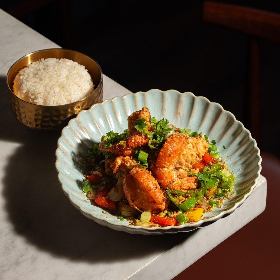 Crispy shrimp and vegetables garnished with herbs in a scalloped bowl, served alongside a bowl of white rice on a marble table.