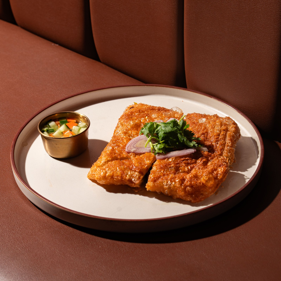 Two golden-brown crispy pastries topped with cilantro and red onion, served with a cup of pickled vegetables on a plate.
