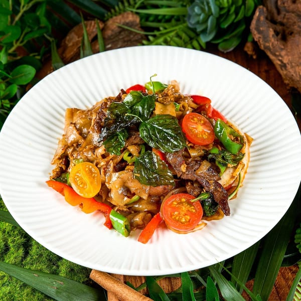 Khaosan's Thai drunken noodles with beef, basil, bell peppers, and cherry tomatoes on a white plate.