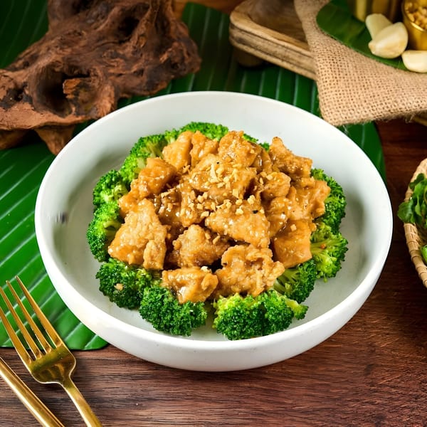 Thai chicken with peanut sauce and broccoli florets in a white bowl on a wooden table.