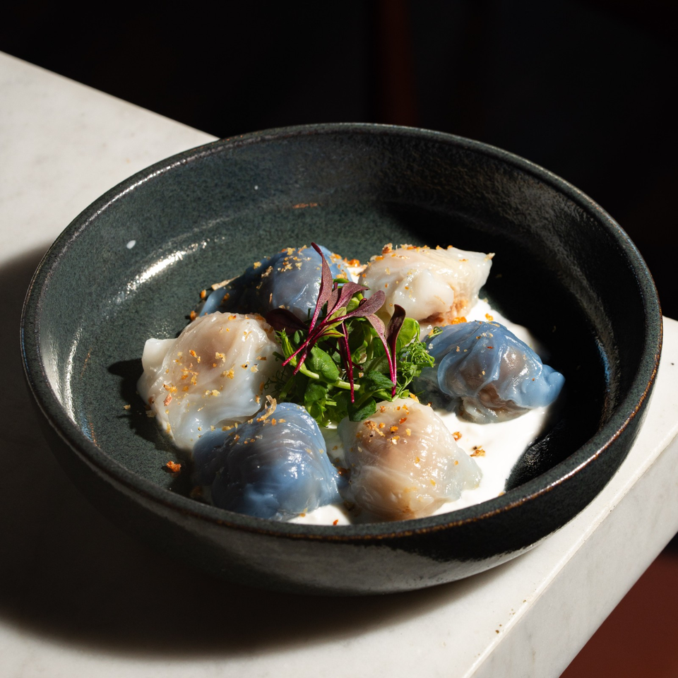 Colorful steamed dumplings with greens and crispy garnish in a dark ceramic bowl.